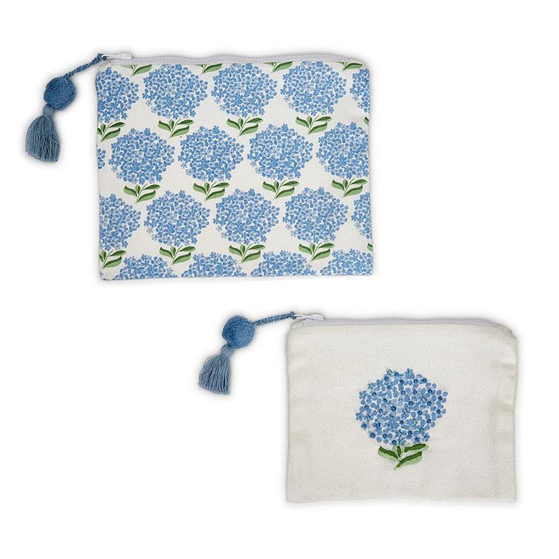 Two zipper poucjhes with blue pom poms attached to the zipper pulls. The larger of the 2 puches has a repeating hydrangea print, while. the second has one embroidered hydrangea on a white background.